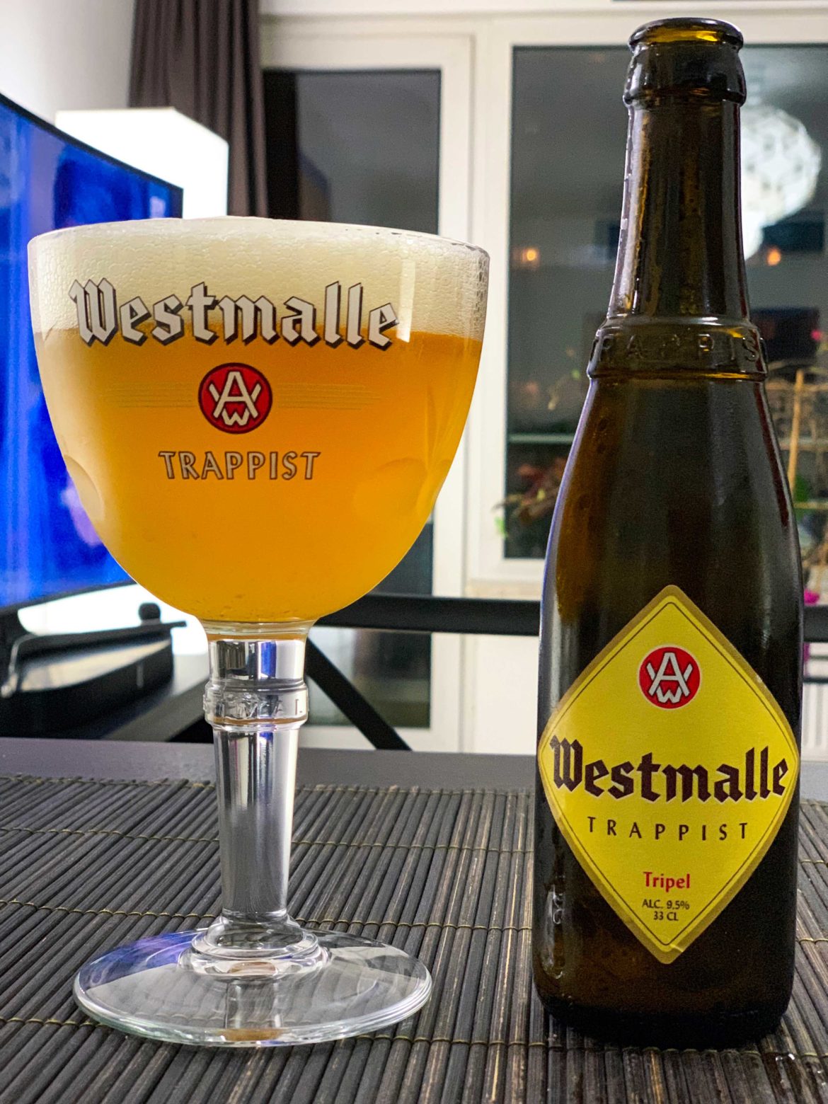 Westmalle Tripple poured in a glass with it's bottle on the side